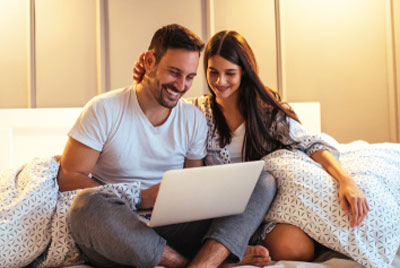 smiling couple sitting in bed with a laptop